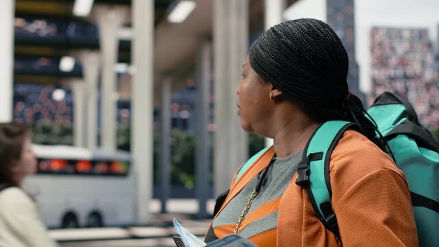 Close-up woman reading travel document details on her phone in the bus station, comparing printed boarding information with the route shown on her smartphone before departure.