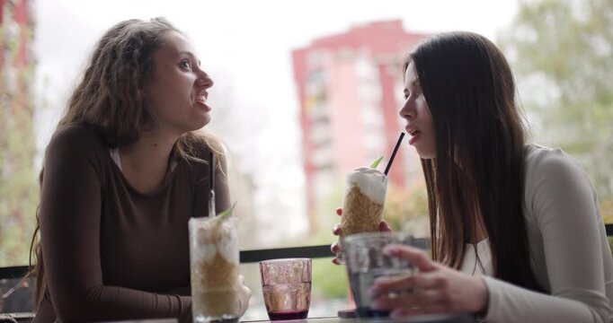Two Friends Sharing Laughter and Conversation Over Drinks at a Cafe