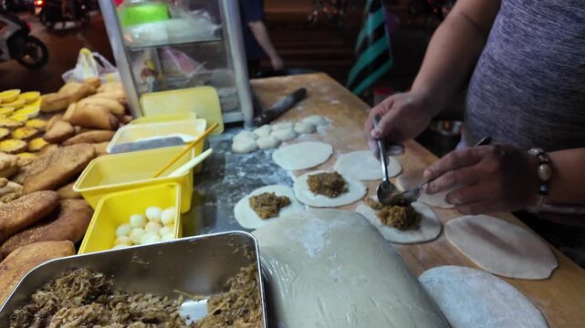 Close up video of a street vendor scooping savory minced pork and wood ear mushroom filling onto fresh dough wrappers to make traditional deep fried buns (banh bao chien) in Ho Chi Minh City, Vietnam