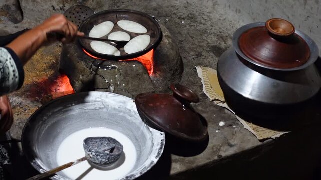 A woman brings out the finished Chitai Pitha in a hot clay oven. Chitai pitha is being made in a terracotta mold for making pitha in a heated clay oven.