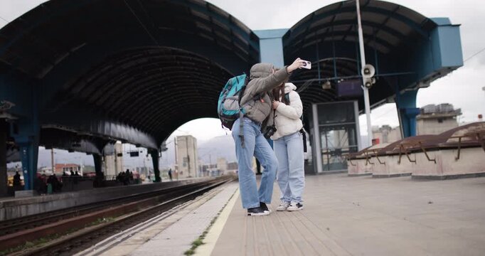 Two Young Women Taking a Selfie at a Train Station as They Embark on an Exciting Journey Together