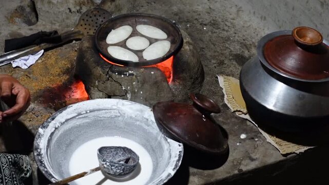 A woman brings out the finished Chitai Pitha in a hot clay oven. Chitai pitha is being made in a terracotta mold for making pitha in a heated clay oven.