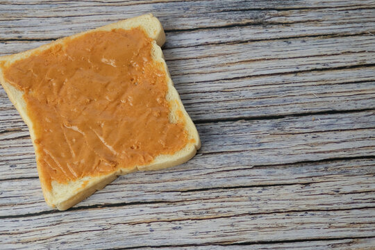 White breads with smooth peanut butter spread. Wooden surface shows gentle texture and natural grain. No people, no animals, no plants in this image. Ideal for breakfast, healthy eating