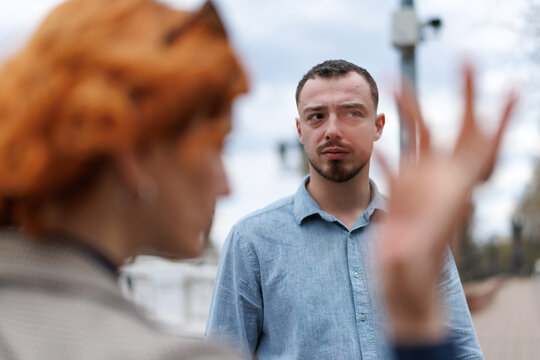 Couple arguing outdoors, frustrated man confronted by woman during tense relationship disagreement on city street