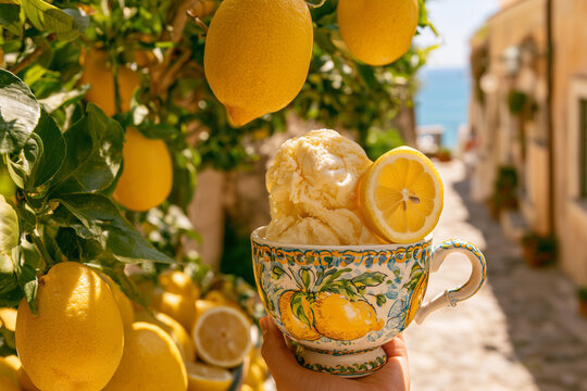 Creamy homemade lemon gelato served in an elegant ceramic cup decorated with hand-painted lemon illustrations, surrounded by fresh lemons beneath a lemon tree