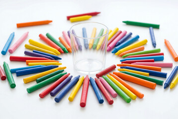 Fototapeta premium Colorful crayons arranged in a circle around an empty glass