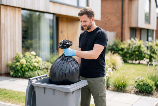 Man throwing a black garbage bag into a grey trash bin