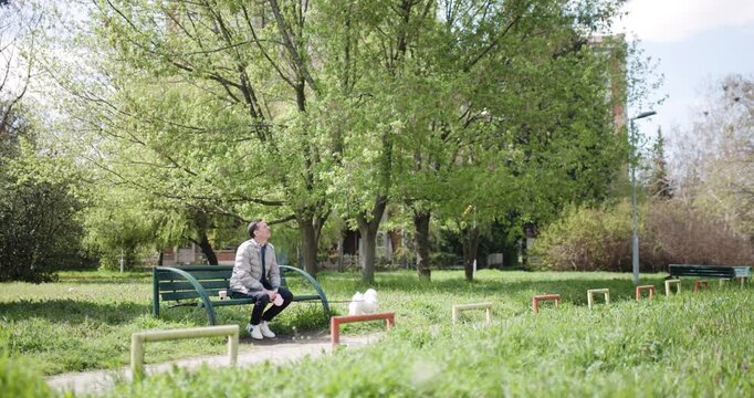 A man sits quietly on a bench in a lush park, appreciating the serene environment and vibrant greenery around him during a sunny spring day