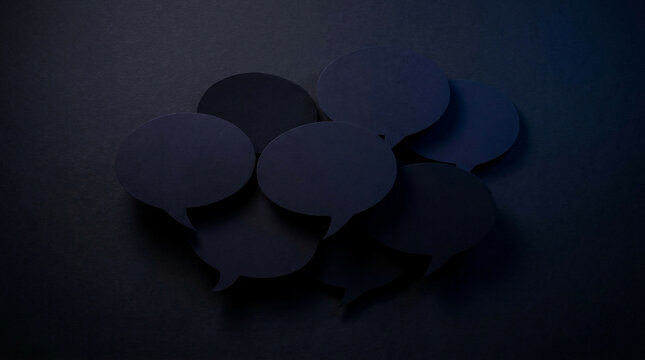 Group of dark blue paper speech bubbles overlapping on a black background, top view, concept for communication, dialogue and discussion