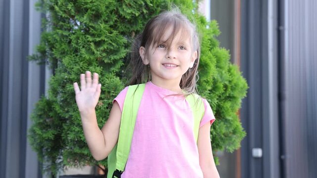 Little girl with backpack waving goodbye outdoors