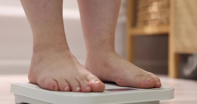 Overweight woman stepping on scale at home, closeup