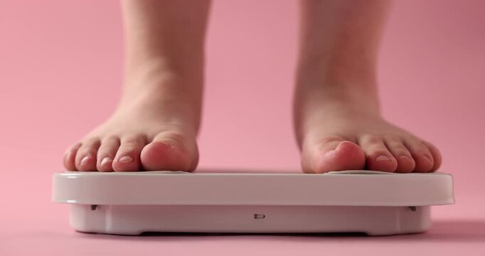 Overweight woman on scale against pink background, closeup