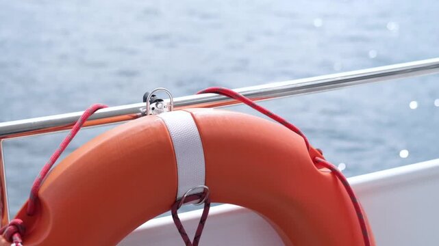 Bright orange life buoy secured to a boat railing with a metal clip, showcasing the tranquil water surface and reflections in the background