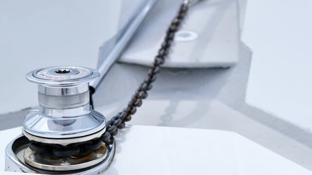Close-up view of a boat winch with chain and anchor line, showcasing the gradual movement of the chain across the deck in a marine setting
