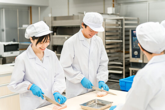 Male and female staff in chef's coats preparing chicken (cooks, chefs, fresh food market workers, food processors)