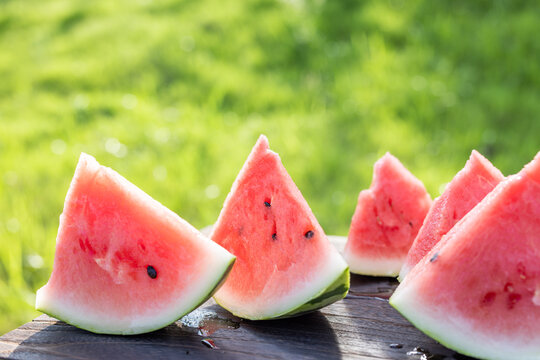 Sliced watermelon pieces on wooden table with green grass background in summer