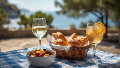 Mediterranean Feast: A delightful spread of crusty bread, olives, and refreshing beverages served on a blue and white checkered tablecloth, overlooking a picturesque coastal landscape. © tienuskin