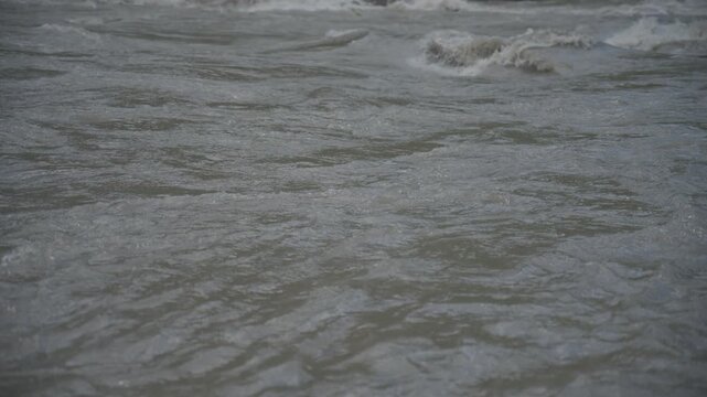Dark grey river waters rushing swiftly past a rocky shore with lush green mountain trees lining the background