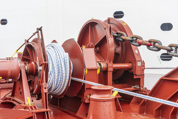 Close-up of a large mooring and anchoring winch installed on the foredeck of a commercial cargo ship, with a thick mooring rope neatly wound around the drum. © Mariusz