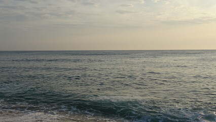 Fototapeta premium Serene Ocean View Under Soft Early Morning Sky. A calm blue sea with subtle wave motion under a soft morning sky shortly along the East Coast of Gangneung, South Korea.