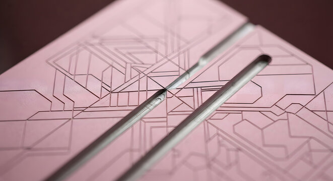 Close-up of a pink precision engineering board with CNC milled geometric channels and layout lines