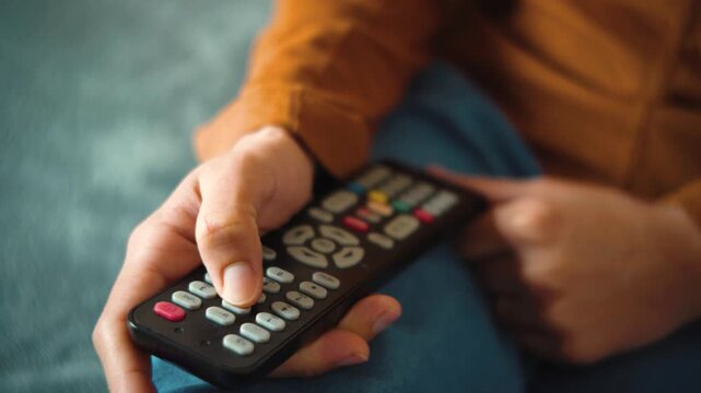 Close-up of an anonymous young woman's hand using a TV remote control while relaxing in bed, representing leisure, entertainment, relaxation, and a cozy moment at home.