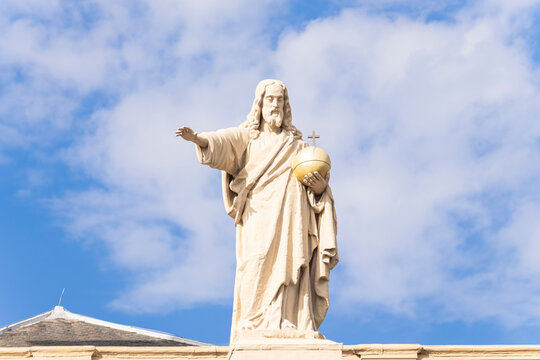 Low angle view of Salvator Mundi stone statue of Jesus Christ with golden globus cruciger against cloudy blue sky backdrop
