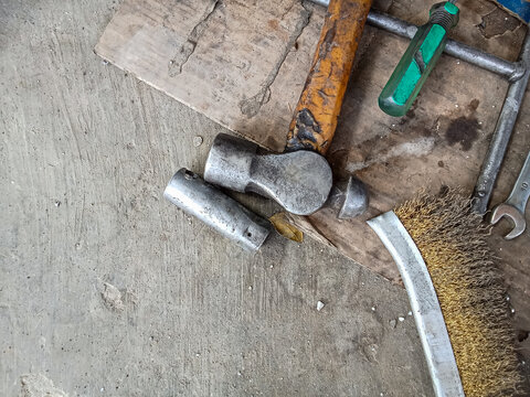 Close-up of old ball-peen hammer with wire brush and socket wrench tools on workshop floor