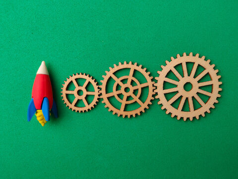 A toy rocket aligned next to three wooden gear cogs on a bright green background