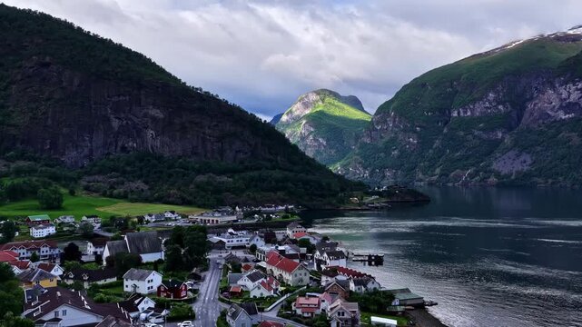 Aerial view of a peaceful fjord village framed by towering peaks and shifting light. Flam, Norway - time lapse while landing