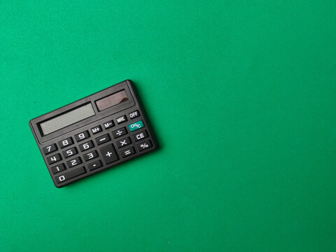 A black electronic calculator positioned on the left side of a wide green surface