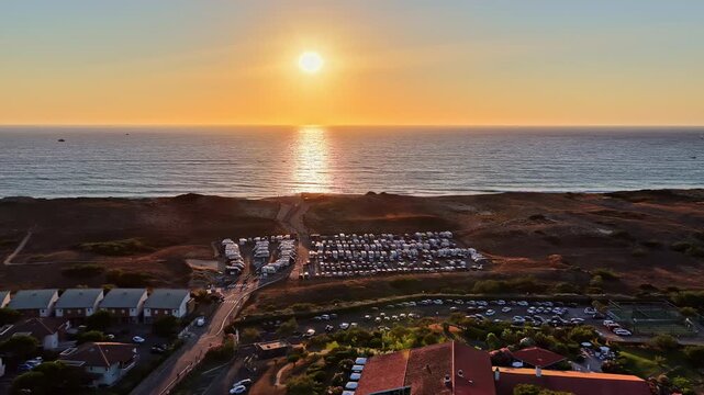 Golden sunset glows over Plage des Oc&eacute;anides beach town with rows of parked campers near ocean
