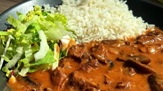 Rich beef goulash in tomato cream sauce paired with rice and lettuce salad