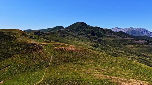 Aerial flyover reveals winding mountain road and hiking trail through green Pyrenees peaks