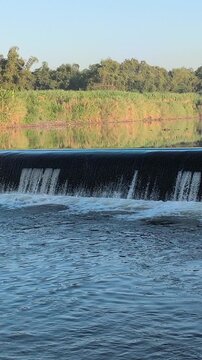 Fast-flowing water rushing over a small dam structure, creating white foam, turbulent currents, and dynamic cascades that highlight the power and movement of flowing water