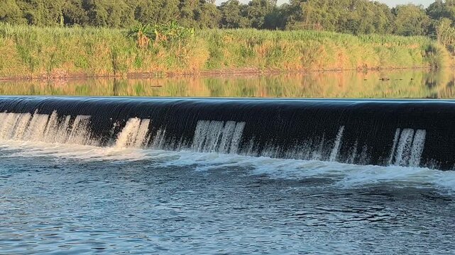 Fast-flowing water rushing over a small dam structure, creating white foam, turbulent currents, and dynamic cascades that highlight the power and movement of flowing water