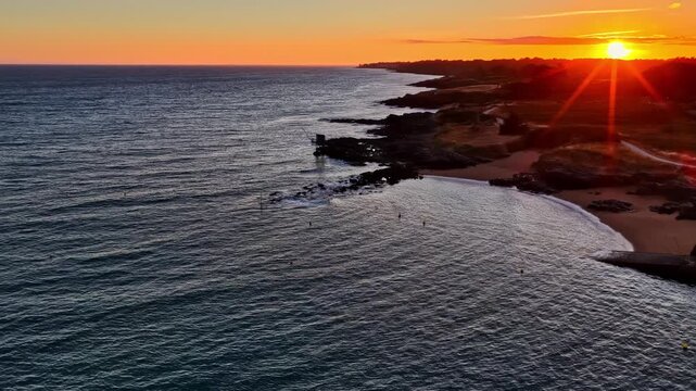 Aerial view approaching a traditional wooden fishing hut on stilts on a rocky coast at sunset