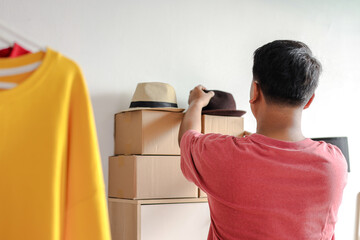 Obraz premium Rear View of Asian Man Arranging Hats and Package Boxes on Shelf for Online Store Business
