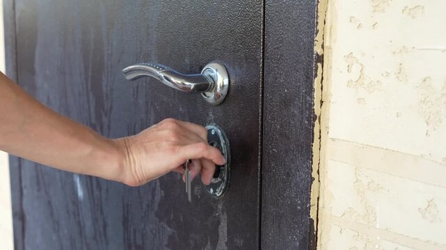 Close up of a hand unlocking and opening a metal door with a key