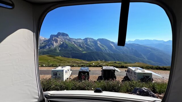 Person relaxing inside a camper van with panoramic mountain views on a clear day