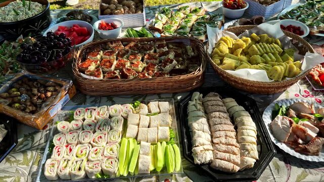 Large outdoor buffet table spread with appetizers, sandwiches, fruit, cold cuts, sausages and salads set on grass for garden party
