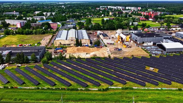 Rows of ground mounted solar panels border an active construction site and warehouses as the camera flies past the complex.