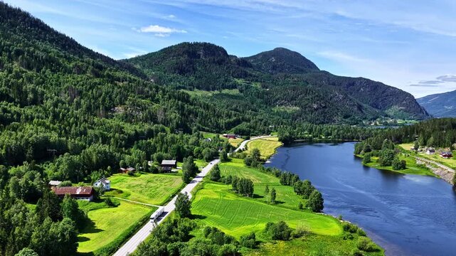 A Scenic Road Winds Through Green Fields Beside a Peaceful Lake Along the Route From Fl&aring;m to Oslo, Norway - Aerial Drone Shot