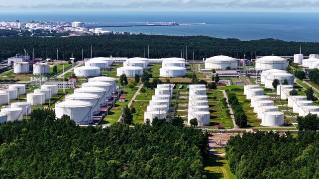 Aerial view of Vitol oil storage terminal in Latvia with rows of tanks surrounded by forest and Baltic Sea coastline