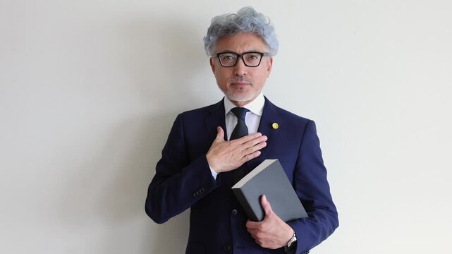 胸に手を当て法律書を持つ信頼感のある中高年の男性弁護士