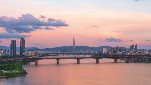Han river reflects pink sunset sky as Seongsu bridge and Lotte tower rise above Seoul skyline in zoom out timelapse