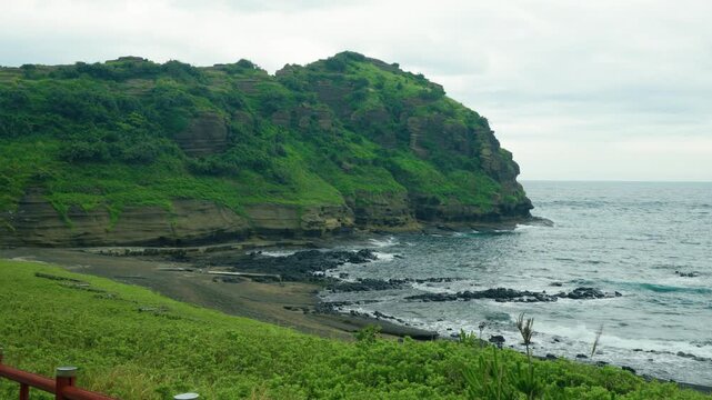 Layered volcanic tuff cliffs rise above rocky cove and gray sand beach at Yongmeori coast in Jeju