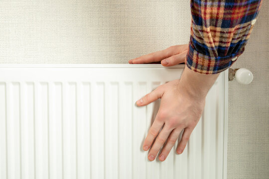 Heating season. Man touches radiator in a warm home, ensuring comfort in cold weather