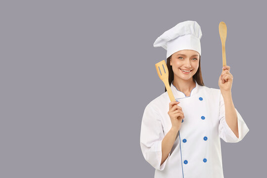 Woman smiles while holding spatula and spoon in kitchen