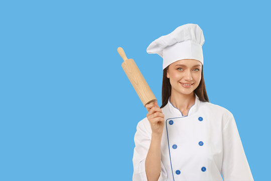 Woman in chef outfit stands smiling and holds a rolling pin
